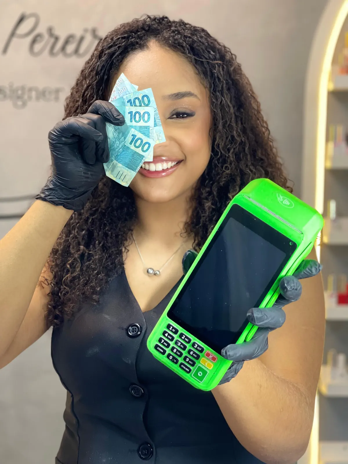Deborah sorrindo, de luvas pretas, segurando notas de cem reais e uma maquininha de cartão